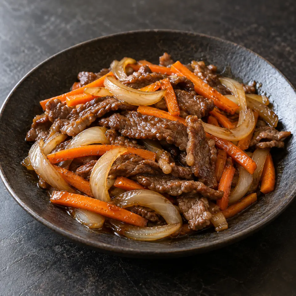 Beef Samgyupsal on a plate on a dark stone table, made with amir's beef striploin steak, carrots, onions, soy sauce.