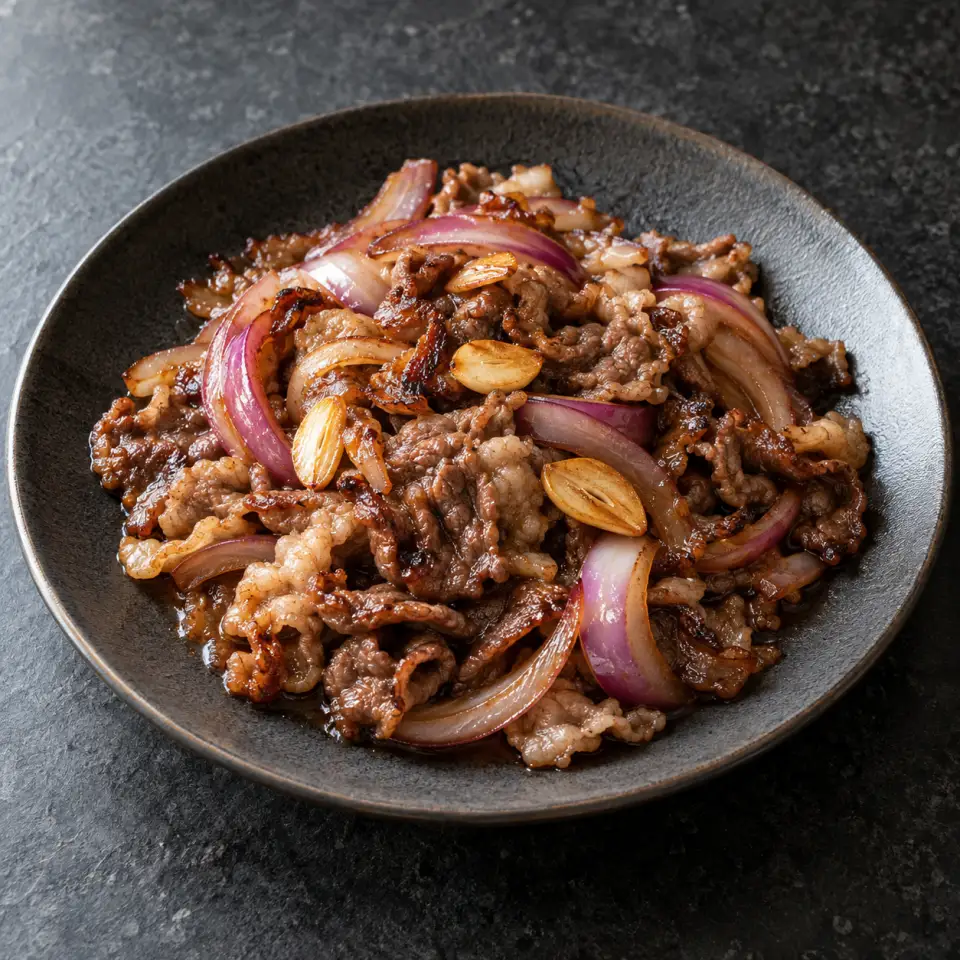 Beef Yakiniku on a plate on a dark stone table, made with beef brisket yakiniku, red onion, garlic.