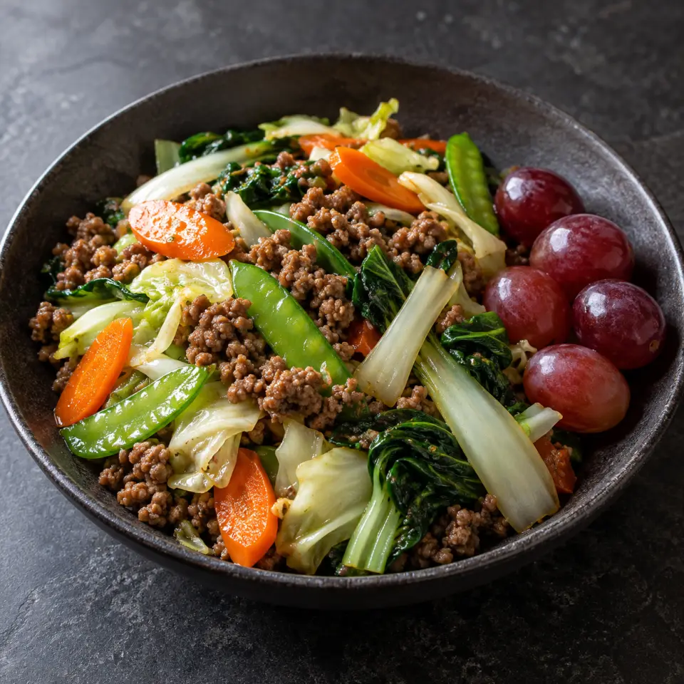 Grapes and Beef on a plate on a dark stone table, made with ginisang pechay, beef ground mexican, mixed chinese vegetables, grapes.