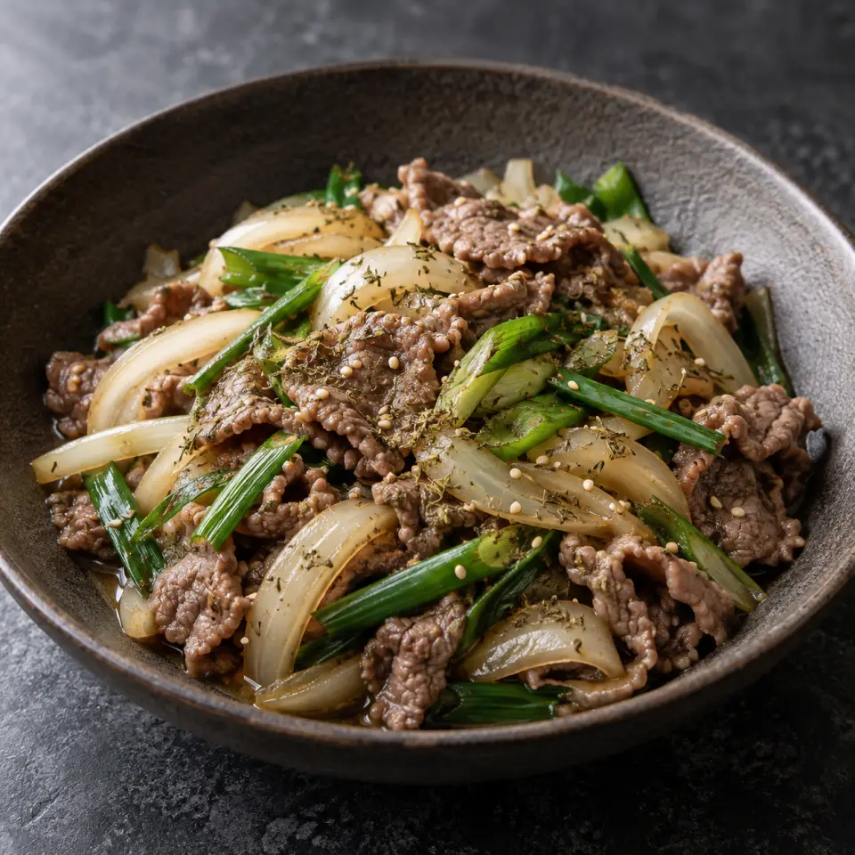 Herbed Beef Sukiyaki on a plate on a dark stone table, made with lean sirloin, white onion, garlic, leaves.