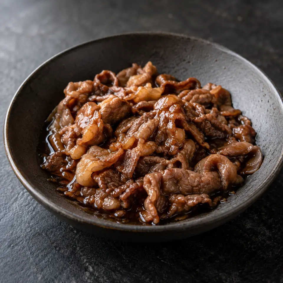 Teriyaki Sukiyaki on a plate on a dark stone table, made with sukiyaki beef, lemon juice, teryaki sauce.