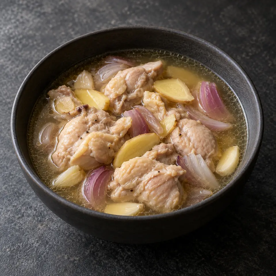 Tinola Manok in a bowl on a dark stone table, made with thigh fillets, red onion, garlic, ginger root.