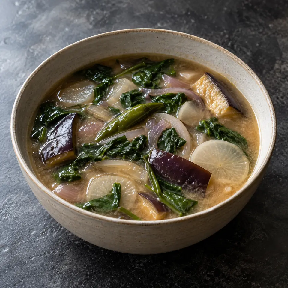 Vegetable Tamarind Miso Sinigang (Sour Soup) in a bowl on a dark stone table, made with eggplant, raddish, pulp, tamarinds.